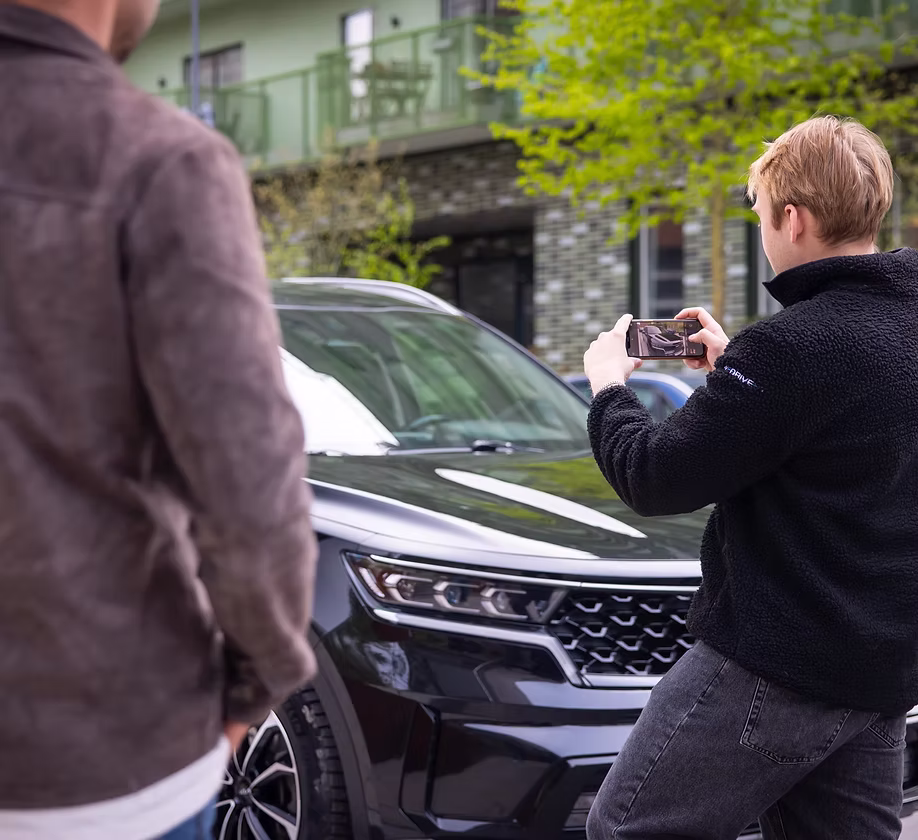 WeDrive-förare fotograferar en svart SUV med mobilen vid överlämning till kund