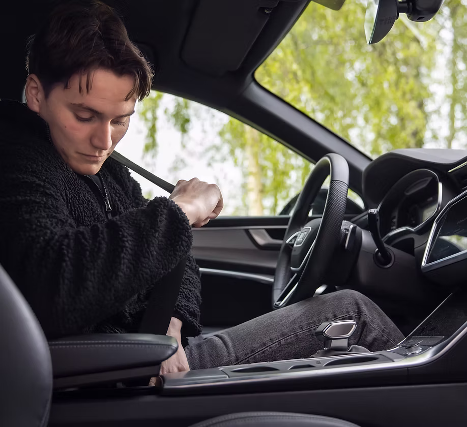 WeDrive-förare i arbetskläder spänner fast bilbältet i förarsätet, grönska utanför rutan