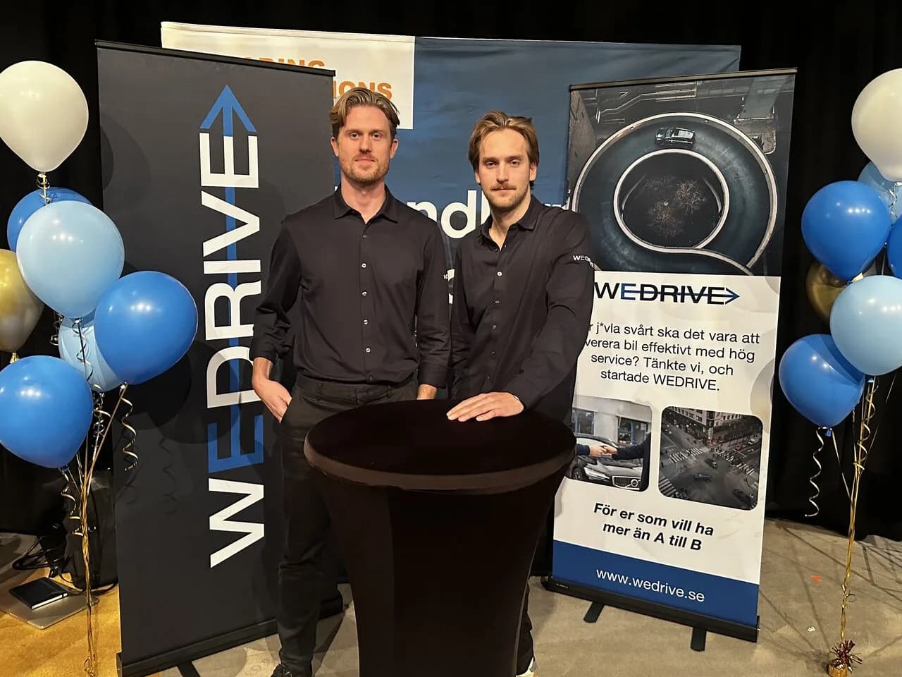 Två personer från WeDrive i svarta skjortor vid WeDrives monter med roll-ups och ballonger