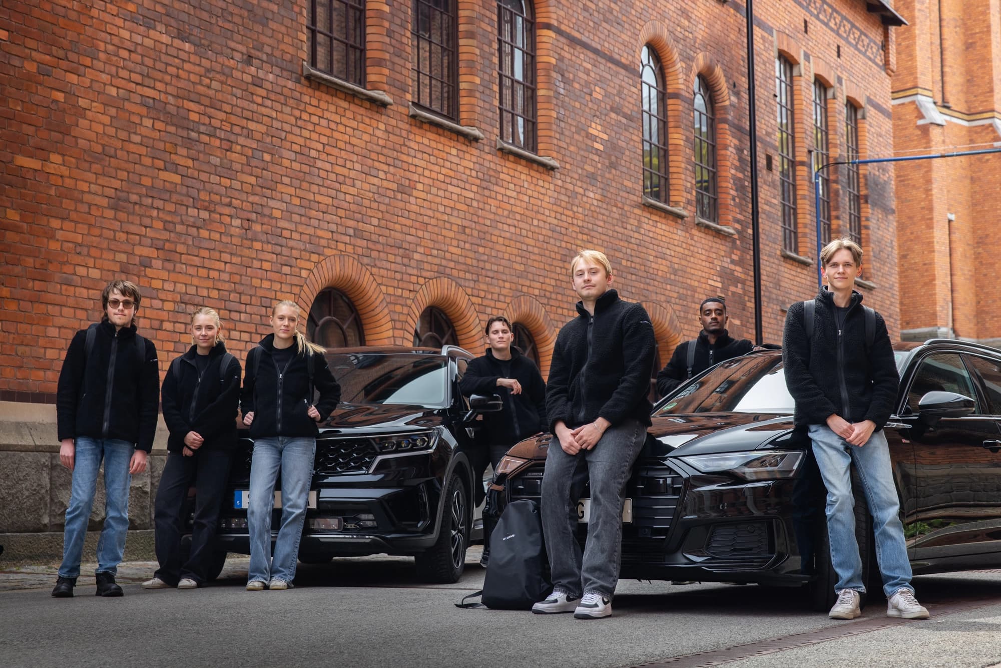 WeDrives drivers framför svarta bilar vid en tegelbyggnad